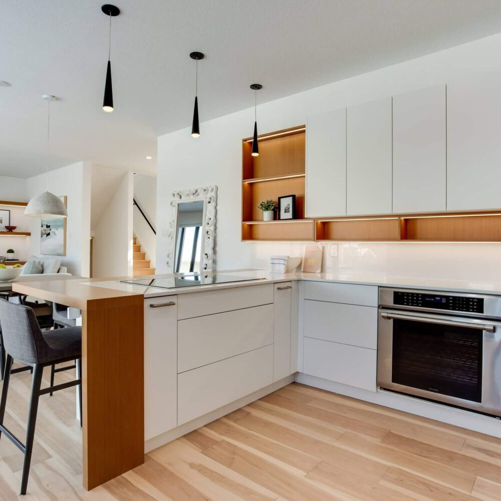 Modern kitchen with white cabinetry, a central island, stainless steel appliances, and wooden accents, featuring pendant lighting and a light wood floor.
