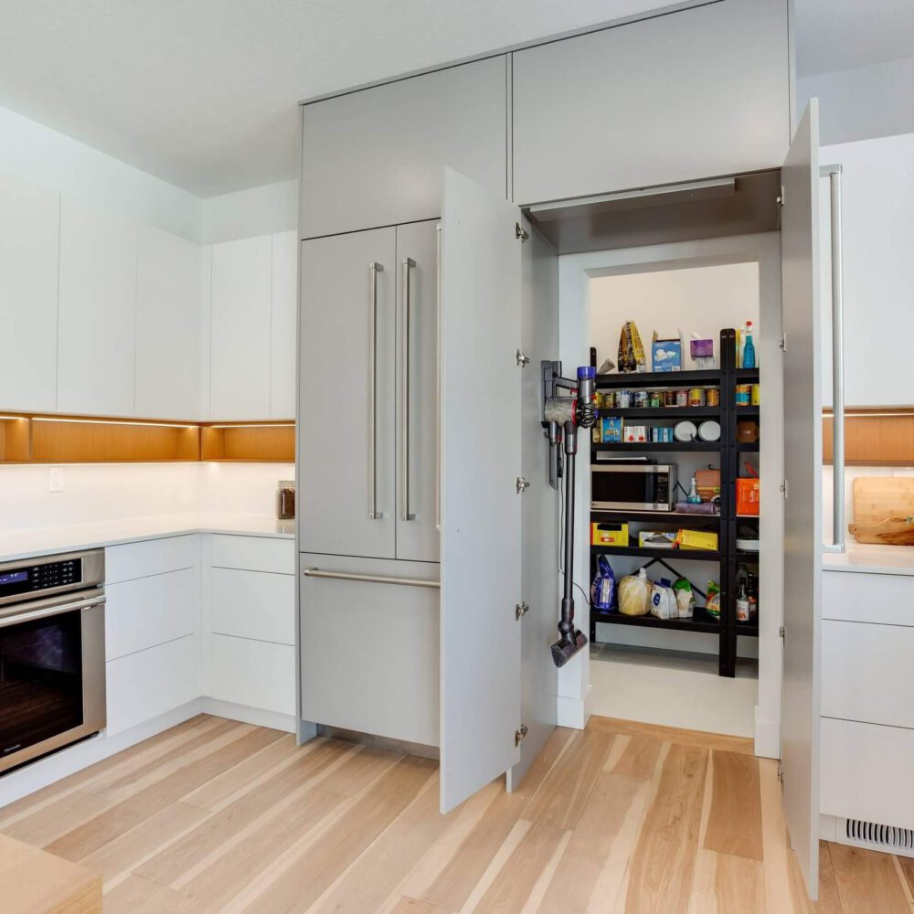 Modern kitchen with sleek cabinetry, an open pantry, and a built-in oven, featuring light wood flooring and minimalist design elements.
