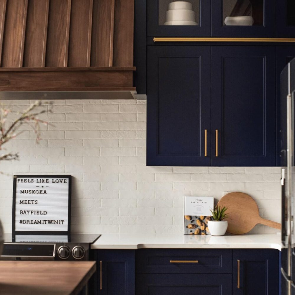 Modern kitchen featuring navy blue cabinetry, white subway tile backsplash, and a wooden cutting board on the counter.