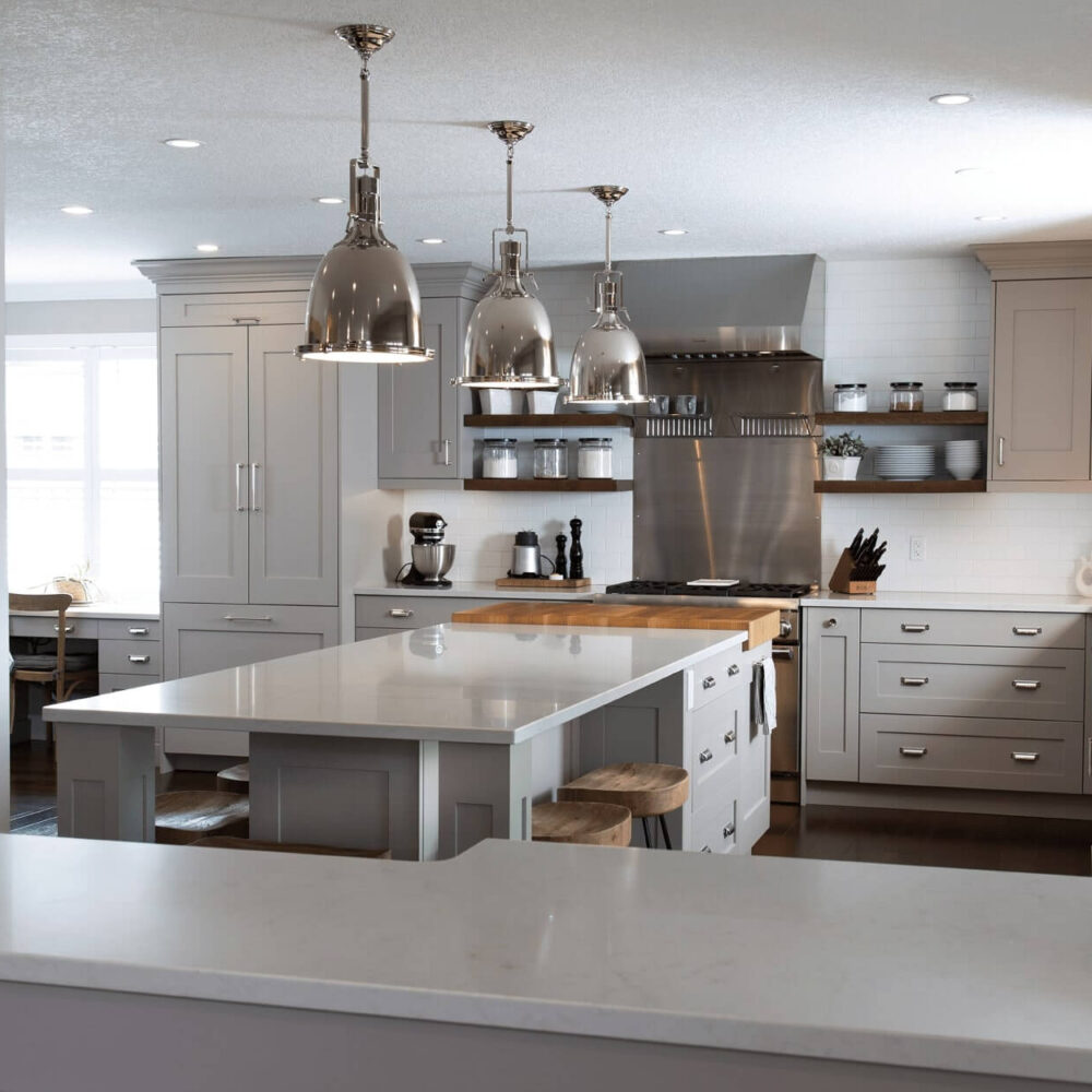 Modern kitchen with gray cabinetry, white countertops, and pendant lighting, featuring an island and stainless steel appliances.
