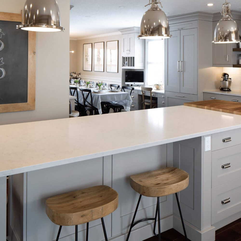 Modern kitchen with a large white countertop island, wooden bar stools, and stainless steel appliances.