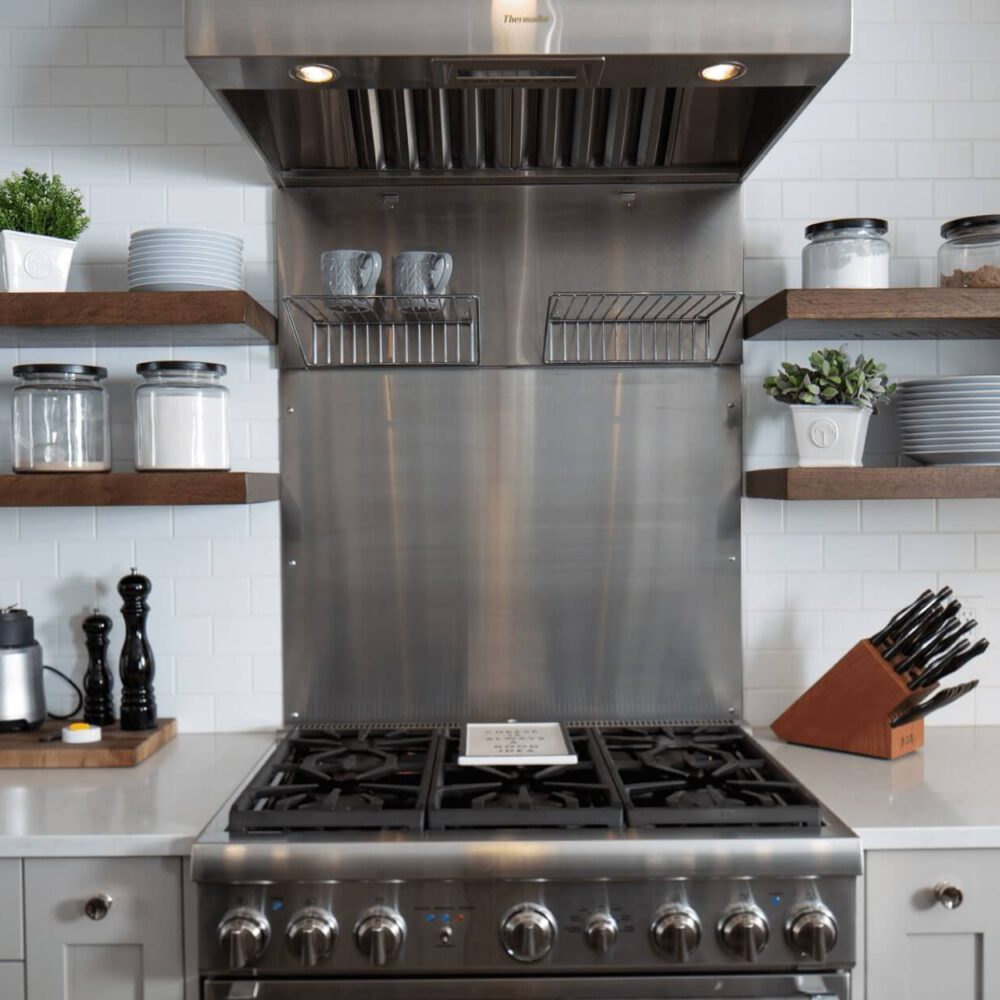 Stainless steel kitchen range with a hood, open shelves displaying glass jars and plates, and a knife block on a countertop.