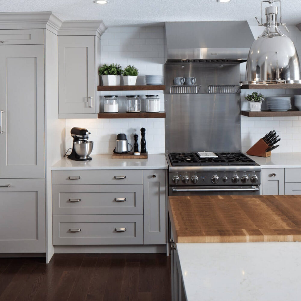 Modern kitchen with gray cabinetry, stainless steel appliances, and a wooden countertop. Features a gas range, mixer, and open shelving.