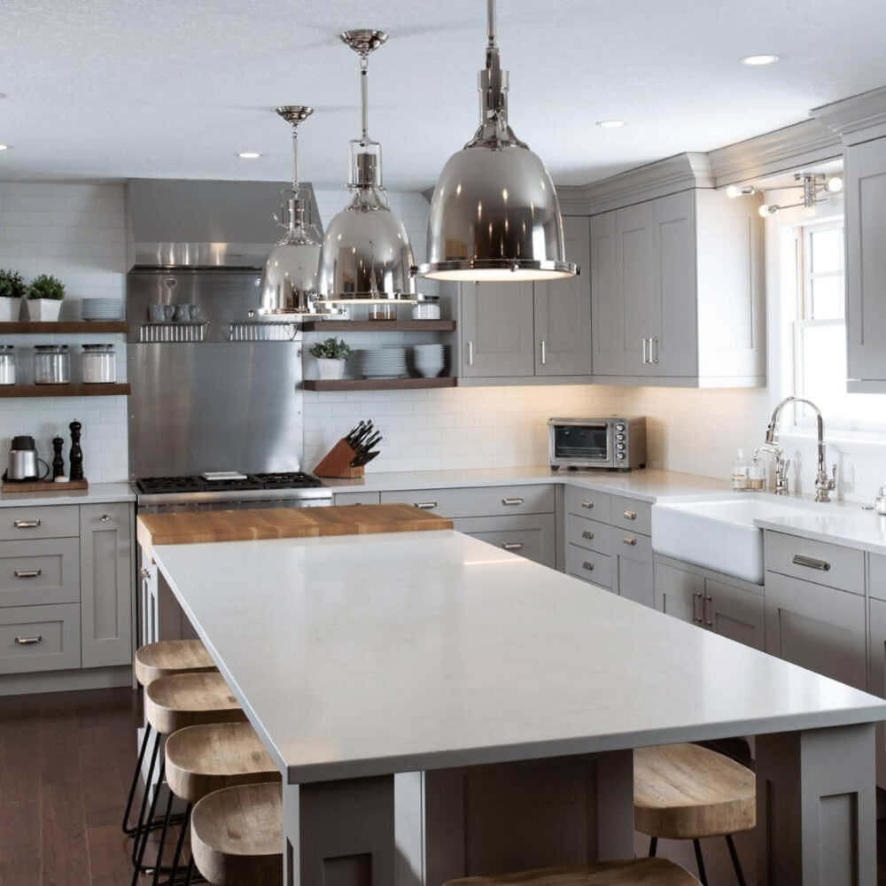 Modern kitchen with gray cabinetry, stainless steel appliances, and a large island with wooden stools.
