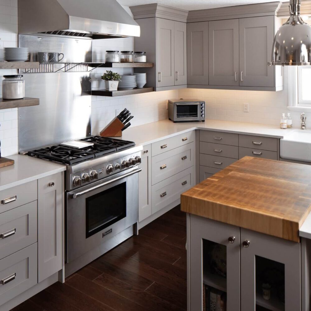 Modern kitchen with gray cabinetry, stainless steel appliances, and a large wooden island with a sink.