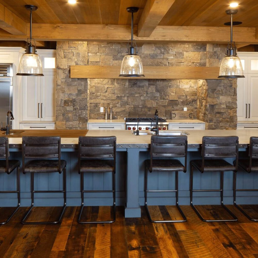 Modern kitchen with a stone accent wall, featuring a large island with six dark bar stools and pendant lighting above.