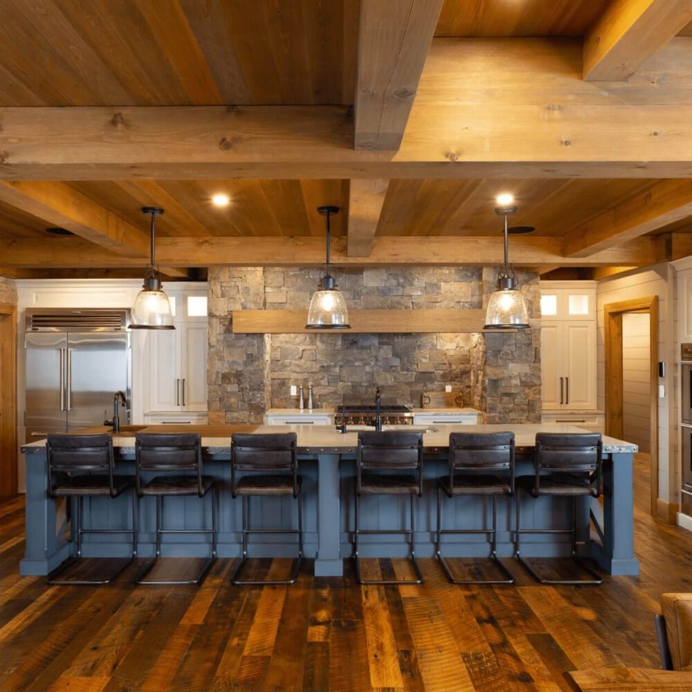 Modern kitchen featuring a large island with bar stools, wooden beams, stone accents, and stainless steel appliances.