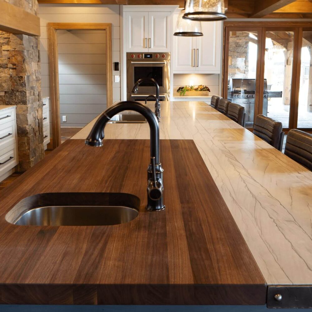 Wooden kitchen island with a sink and a marble countertop, featuring modern fixtures and a spacious design.