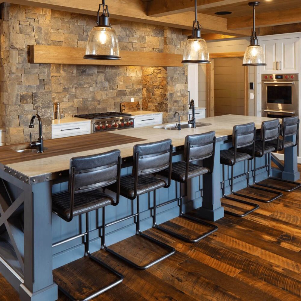 Modern kitchen with a large island featuring wooden countertops and bar stools, stone wall, and stainless steel appliances.