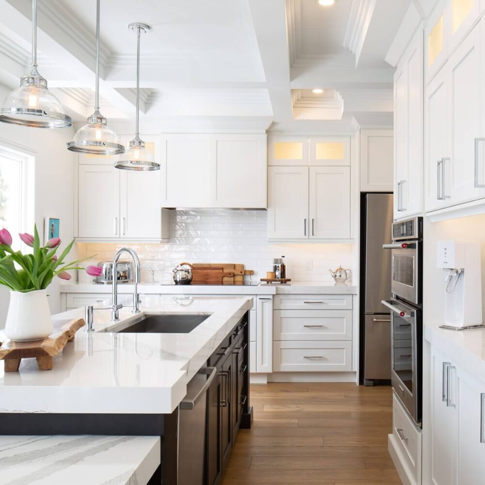 Modern kitchen with white cabinetry, quartz countertops, and pendant lighting, featuring a sink and a vase of tulips on the island.