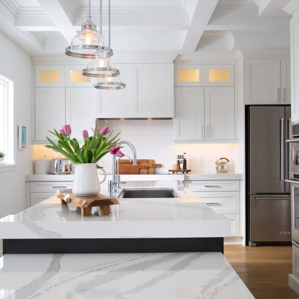 Modern kitchen with white cabinetry, stainless steel appliances, and a marble countertop adorned with a vase of tulips.