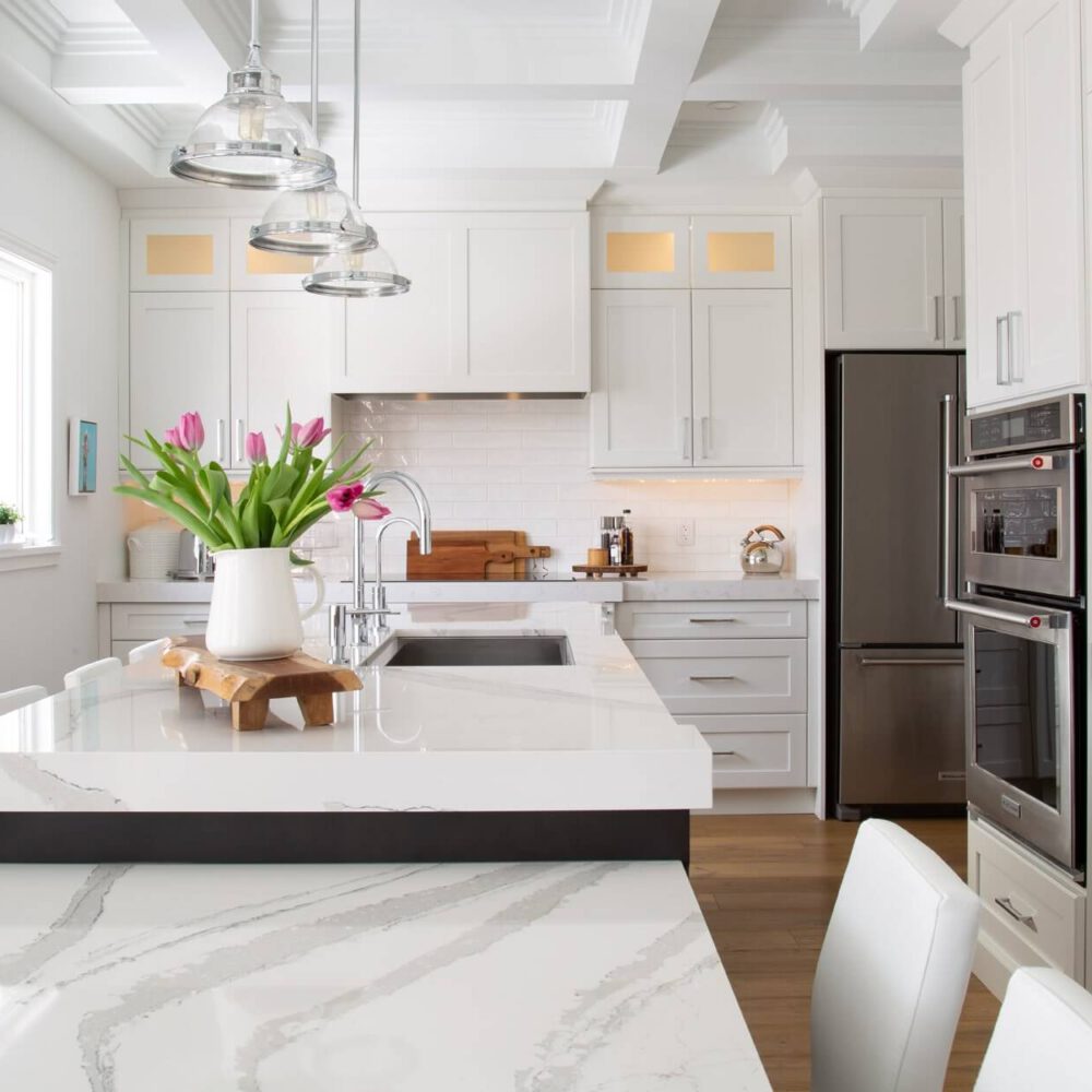 Modern kitchen with white cabinetry, stainless steel appliances, and a marble countertop featuring a vase of tulips.