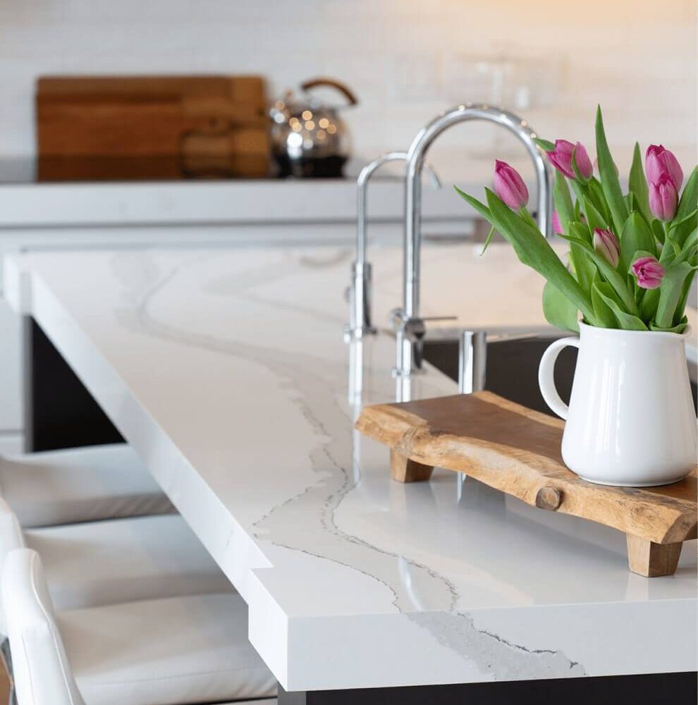 Modern kitchen countertop with a white surface featuring gray veining, a wooden serving board, and a vase of tulips.