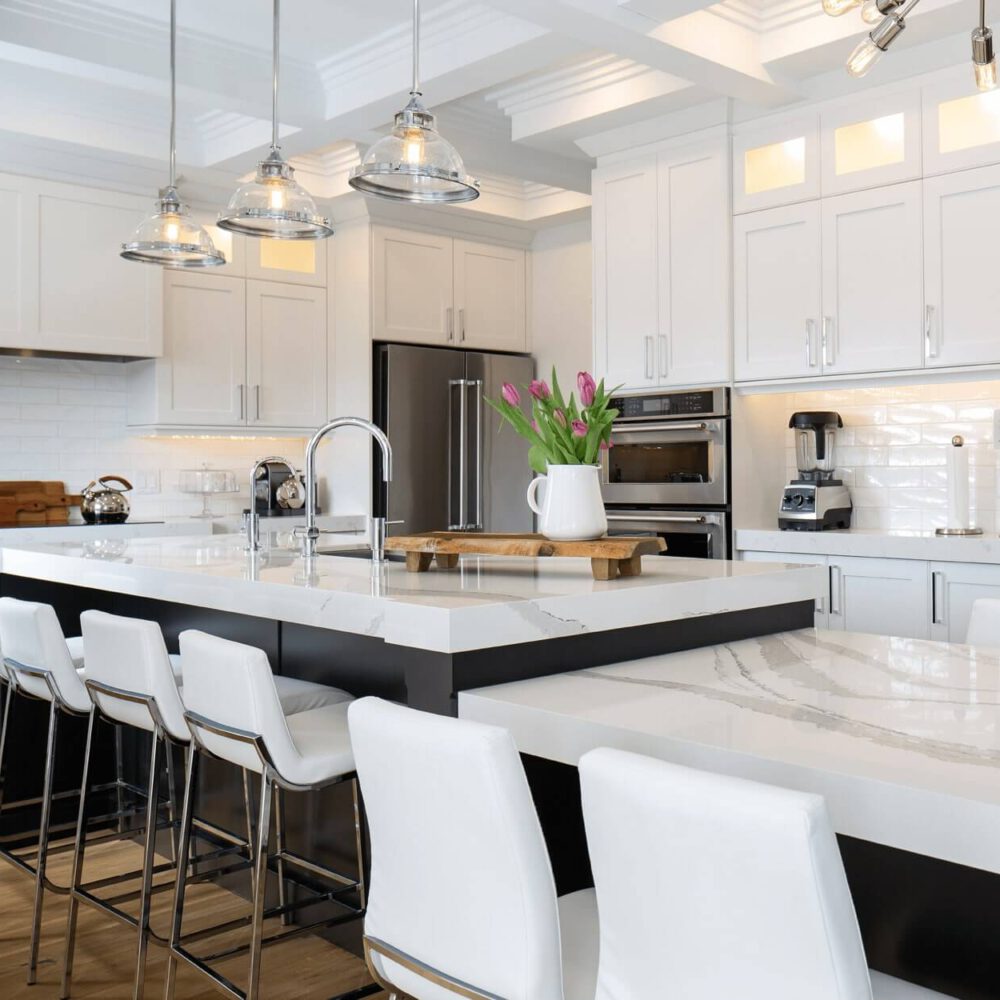 Modern kitchen with white cabinetry, a large island with a marble countertop, and stainless steel appliances.