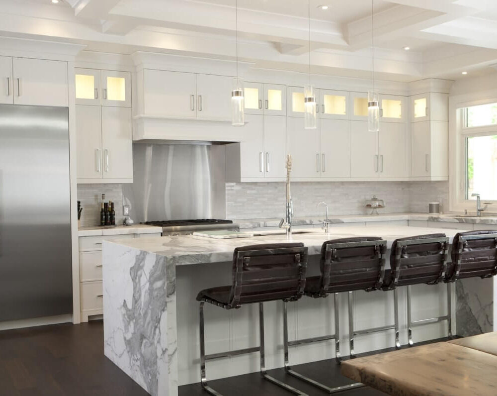 Modern kitchen with white cabinetry, stainless steel appliances, and a marble island with bar stools.