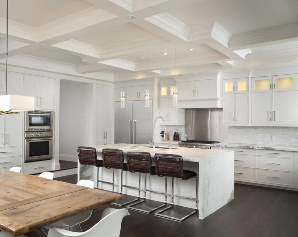 Modern kitchen with white cabinetry, marble island, stainless steel appliances, and wooden dining table with white chairs.
