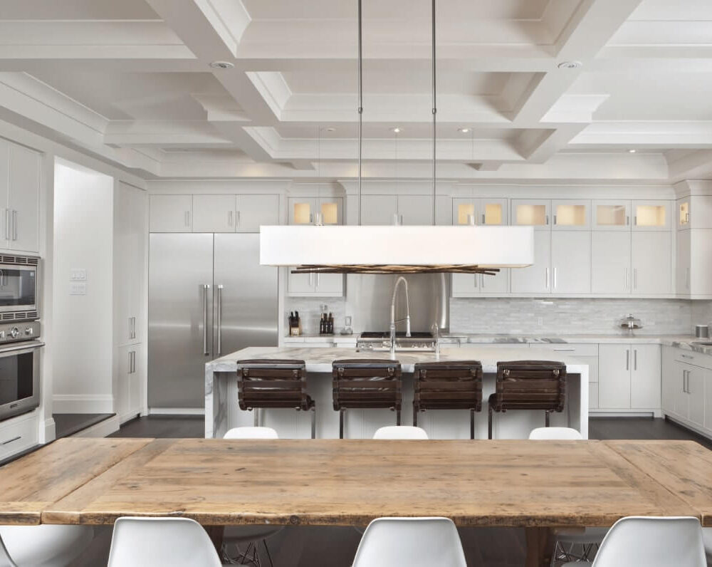Modern kitchen with white cabinetry, stainless steel appliances, and a wooden dining table with white chairs.