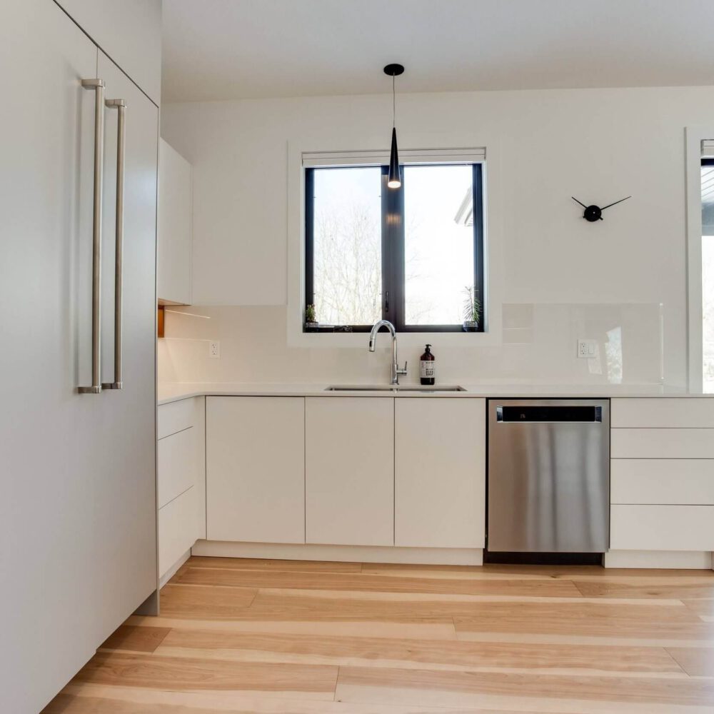 Modern kitchen with white cabinetry, stainless steel dishwasher, and large windows providing natural light.