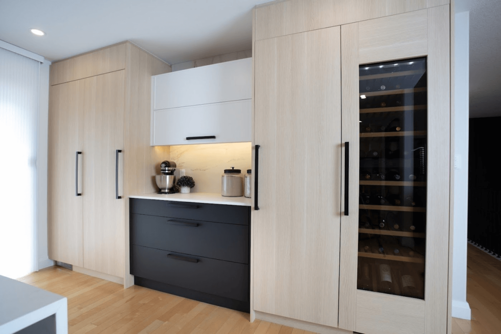 _19A1062+(1) Modern kitchen cabinetry with light wood and black accents, featuring a wine cooler and built-in appliances.