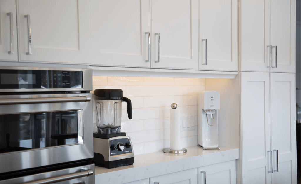 Project_Kitchens_Lexington6 Modern kitchen countertop with a blender, water dispenser, and a paper towel holder against white cabinetry.