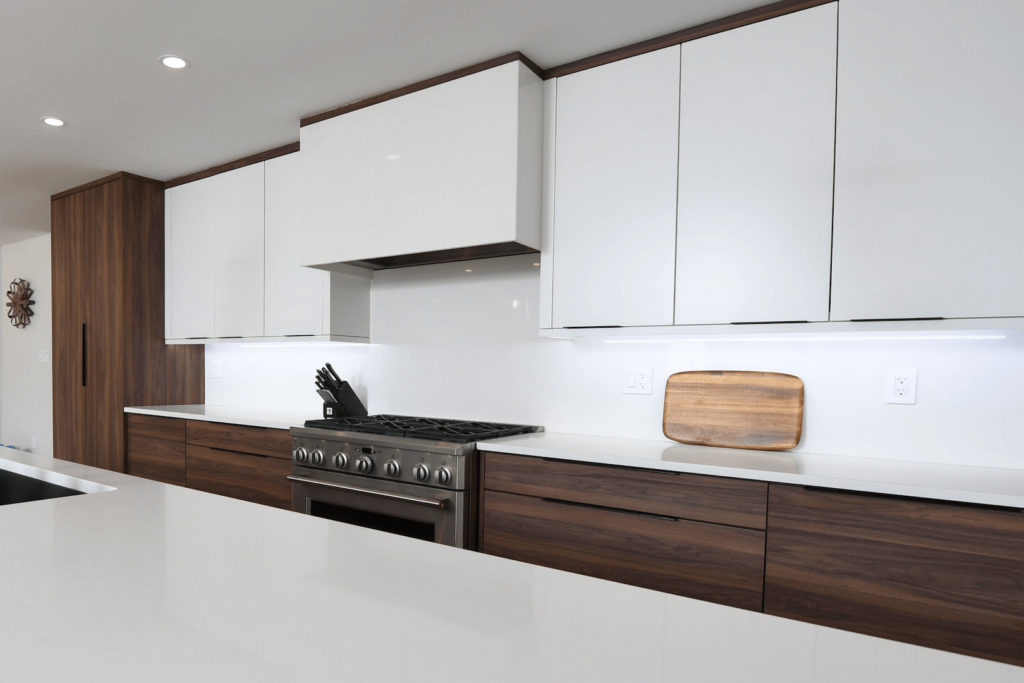 ygLU9l3s Modern kitchen with sleek white cabinetry, wooden accents, a stainless steel stove, and a cutting board on the counter.